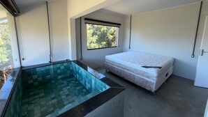 A room with a glass-bottomed pool, a mattress, and a window with a view of greenery.