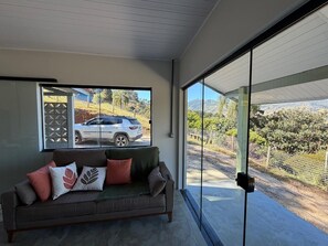 A modern interior with a sofa and a glass door leading to an outdoor area. - Deusmideu Refuge (São Bento do Sapucaí)