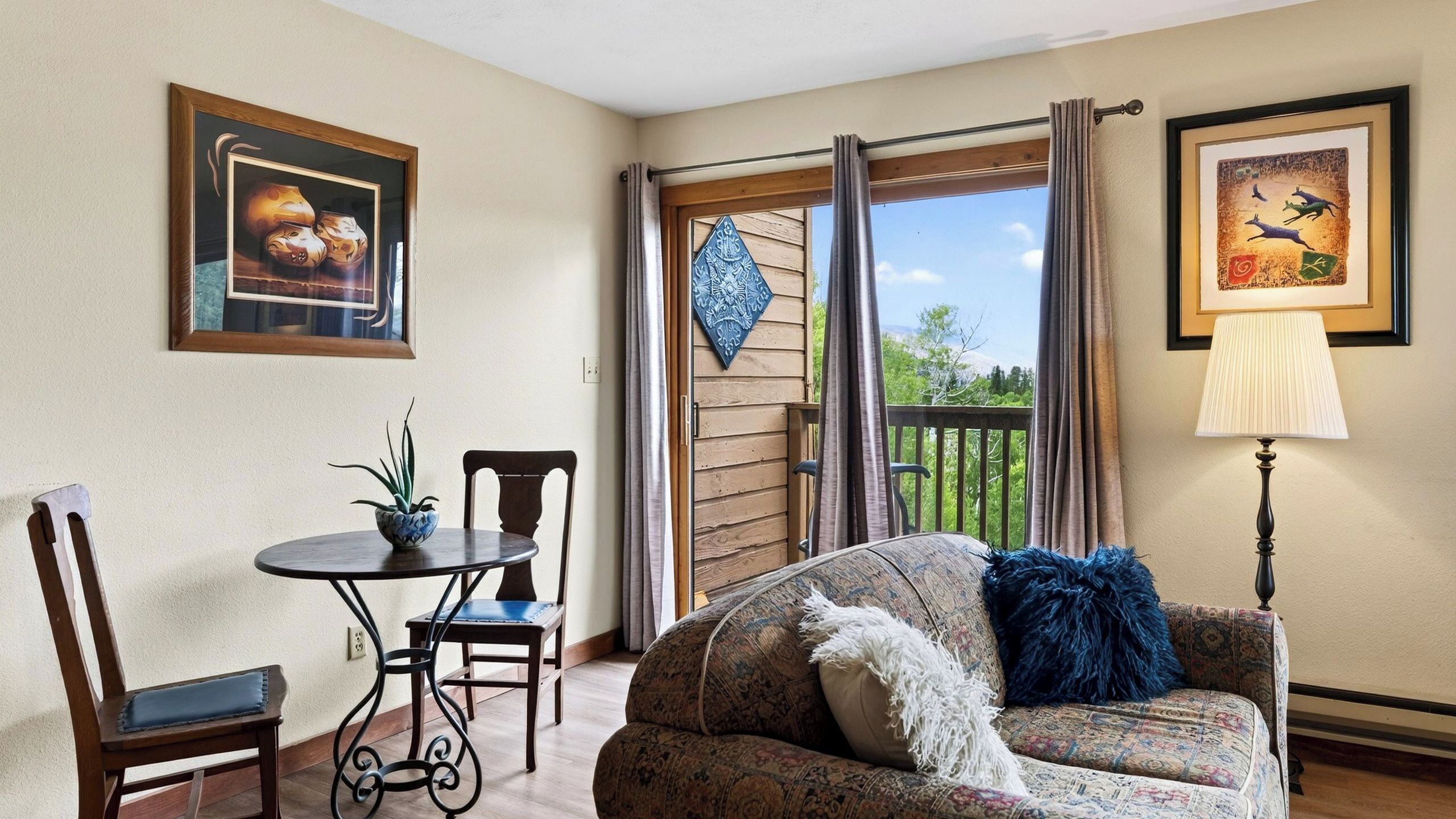 A cozy room with a dining table, chairs, a sofa, a lamp, and a view through a glass door.