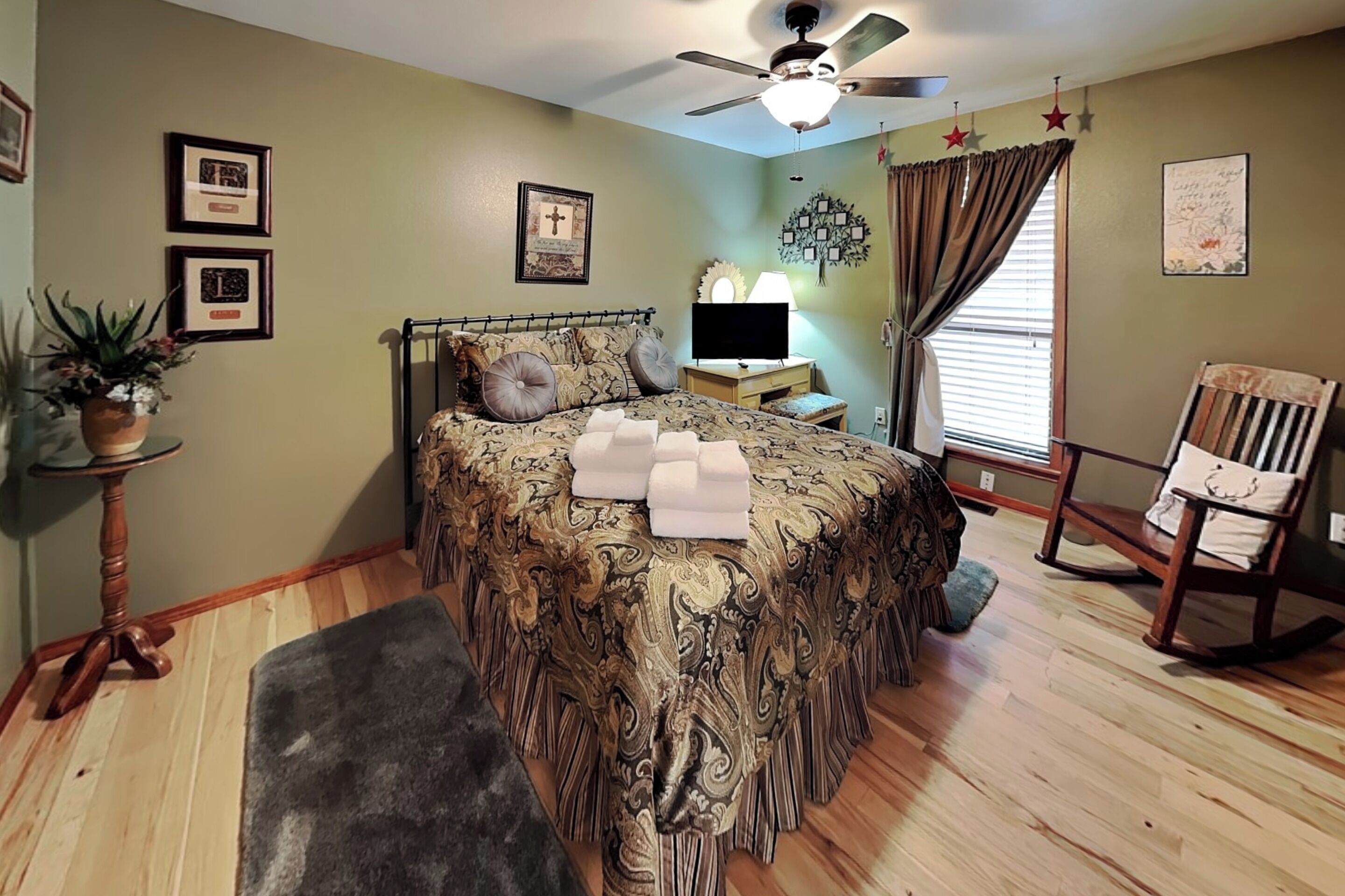 A bedroom with a bed, a chair, a desk, a ceiling fan, and a window with curtains.