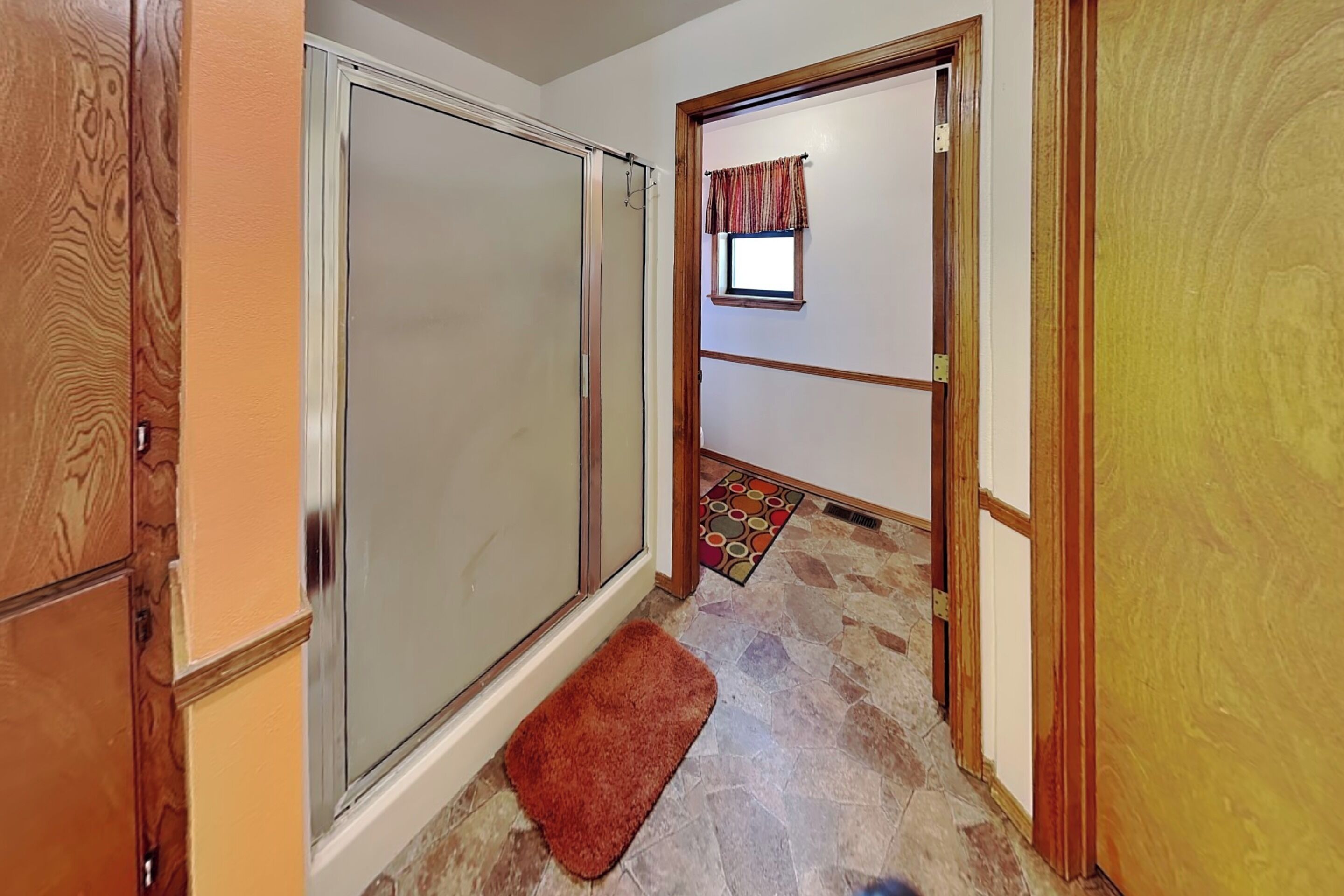 A hallway with a sliding glass door, a small window with a curtain, a rug, and a door with a wooden frame.