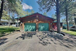 Una baita di legno con due porte garage verdi, immersa tra alberi e un cielo sereno.