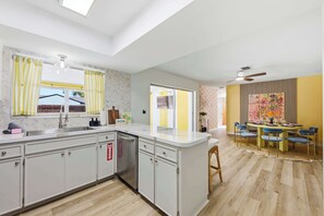 Eine moderne Küche mit einer zentralen Kochinsel, einem Essbereich mit einem gelben Tisch und blauen Stühlen sowie einem Deckenventilator.