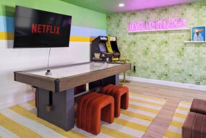 A room with a flat-screen TV displaying 'NETFLIX', a neon sign reading 'LEVEL UP IN LARGO', and a wrestling game machine. - Pool •  Hot Tub•  Putt Putt • Game Room •  Karaoke (Largo)