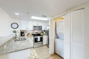 A compact kitchen with white cabinets, a microwave, oven, and a built-in washing machine. - Bay Watch Resort 0241 (North Myrtle Beach)