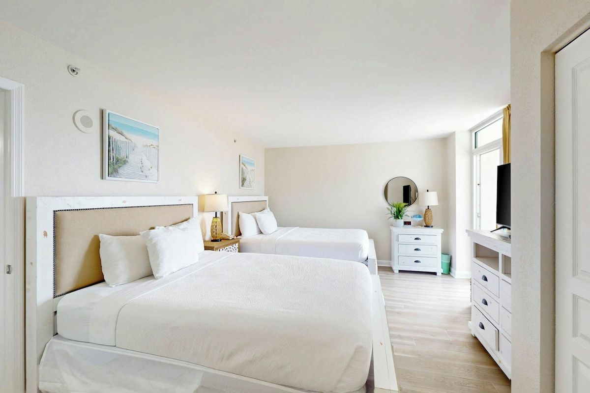 Quarto de hotel com duas camas, televisão, escrivaninha e cómoda.