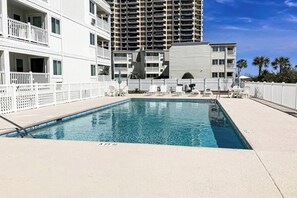 A swimming pool with a white fence, lounge chairs, and a view of a tall building in the background. - A Place at the Beach V - A307 (Myrtle Beach)