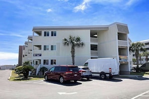 A multi-story hotel with a parking lot, a red car, and a white van. - A Place at the Beach V - A307 (Myrtle Beach)