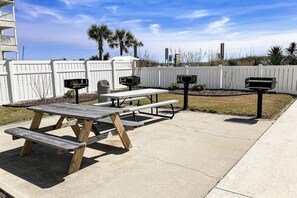 Eine Terrasse im Freien mit einem Picknicktisch, Grillanlagen und einem weißen Zaun.
