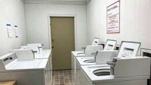 Una lavanderia con diverse lavatrici e asciugatrici, un pavimento piastrellato e una porta alla fine.