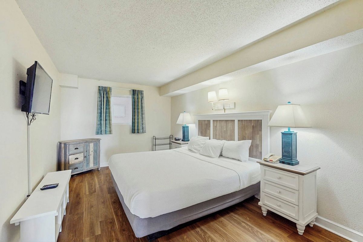 Una habitación de hotel con una cama grande, mesitas de noche, un televisor y un escritorio.