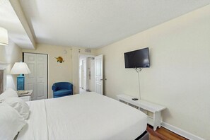 A hotel room with a bed, a television mounted on the wall, a desk with a lamp, and a chair. - Bay Watch Resort 0335 (North Myrtle Beach)