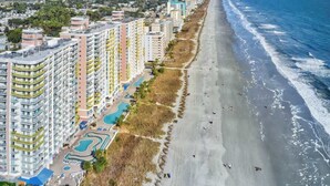 Un hotel frente al mar con varios edificios altos, una playa de arena y una vista despejada del océano.