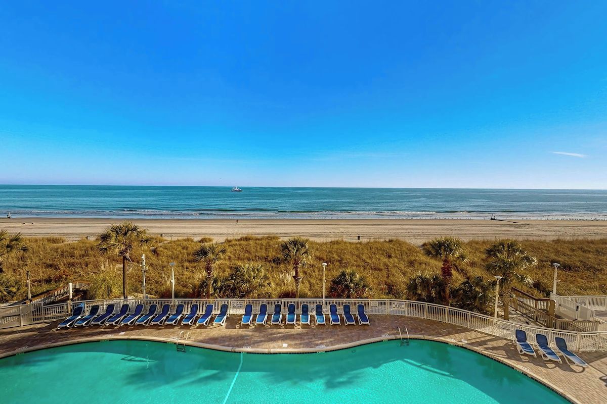 A pool area with lounge chairs and a view of the beach.