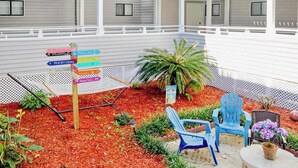 A covered outdoor area with a directional sign, seating, and a small garden. - Arcadian Dunes 02-207 (Myrtle Beach)