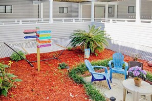 A covered outdoor area with a directional sign, seating, and a small garden. - Arcadian Dunes 02-207 (Myrtle Beach)
