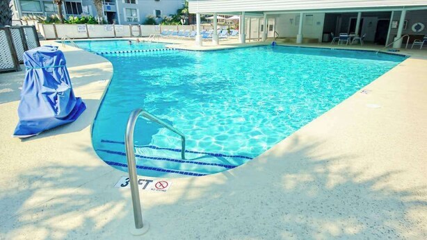 A swimming pool with a metal ladder, a covered area, and a no swimming sign. - Arcadian Dunes 02-207 (Myrtle Beach)
