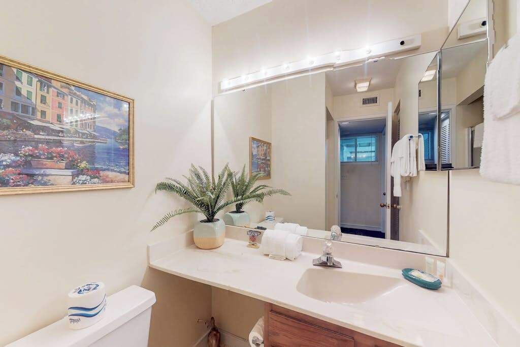 Een badkamer met een grote spiegel, een wastafel, een toilet en een schilderij in een lijst aan de muur.