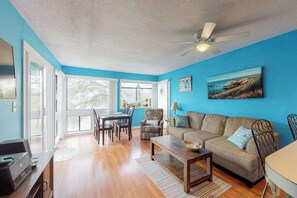 Un salon avec un mur bleu, un ventilateur de plafond, un canapé, une table basse et un coin repas avec des chaises et une table.