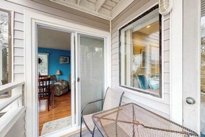 Une véranda couverte avec une table et des chaises, une porte-fenêtre coulissante donnant sur une pièce avec un mur bleu et un lit.