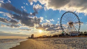 A beach with a large Ferris wheel, ocean, and buildings in the background. - Arcadian Dunes 02-208 (Myrtle Beach)
