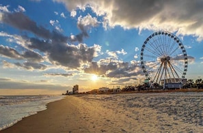 A beach with a large Ferris wheel, ocean, and buildings in the background. - Arcadian Dunes 02-208 (Myrtle Beach)