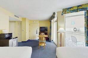 Ein Hotelzimmer mit einem Bett, einem Schreibtisch mit Mikrowelle, einem Fernseher und einem Esstisch mit Stühlen.