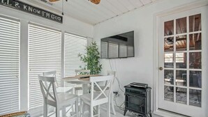 A room with a dining table, chairs, a potted plant, a television, and a door with a window. - Cozy Beach House 314 (North Myrtle Beach)
