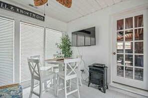 Ein Zimmer mit Esstisch, Stühlen, einer Topfpflanze, einem Fernseher und einer Tür mit Fenster.