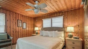 A wooden-paneled bedroom with a bed, two bedside lamps, a ceiling fan, and a nightstand with drawers. - Cozy Beach House 314 (North Myrtle Beach)