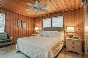 Ein Schlafzimmer mit Holzvertäfelung, einem Bett, zwei Nachttischlampen, einem Deckenventilator und einem Nachttisch mit Schubladen.