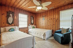 A cabin-style room with two beds, a ceiling fan, wooden walls, and a blue couch. - Cozy Beach House 314 (North Myrtle Beach)
