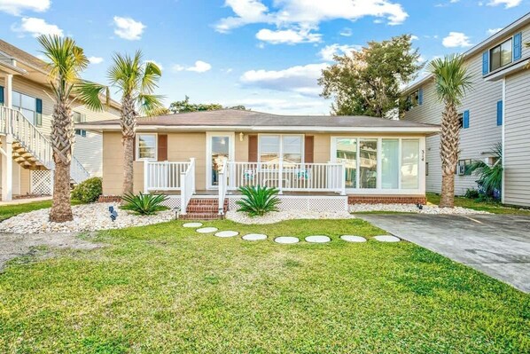 A single-story house with a front porch, a small front yard with palm trees, and a clear sky. - Cozy Beach House 314 (North Myrtle Beach)