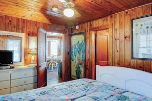 A wooden-paneled room with a bed, a television, a desk with a lamp, and a door leading to another room. - Ocean Gem (North Myrtle Beach)
