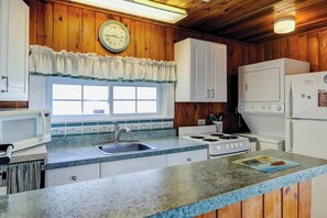 A kitchen with wooden walls, a clock, a window, a sink, a stove, and a refrigerator. - Ocean Gem (North Myrtle Beach)
