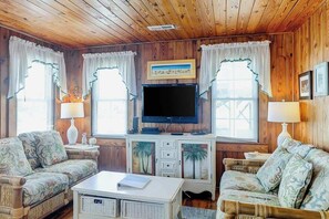 A cozy room with wooden walls, a flat-screen TV, two patterned sofas, a white coffee table, and a cabinet with drawers. - Ocean Gem (North Myrtle Beach)