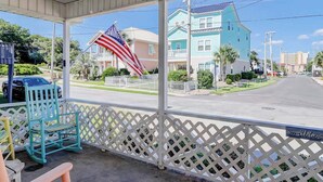 Eine überdachte Veranda mit Blick auf eine Wohnstraße, einem Schaukelstuhl und einer amerikanischen Flagge.