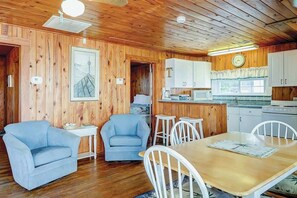 A wooden interior with a dining area, two blue armchairs, a white table, and a kitchen with white cabinets. - Ocean Gem (North Myrtle Beach)