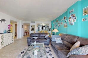 A living room with two sofas, a coffee table, and a wall decorated with photos. - Oceanfront Arcadian II  8D (Myrtle Beach)