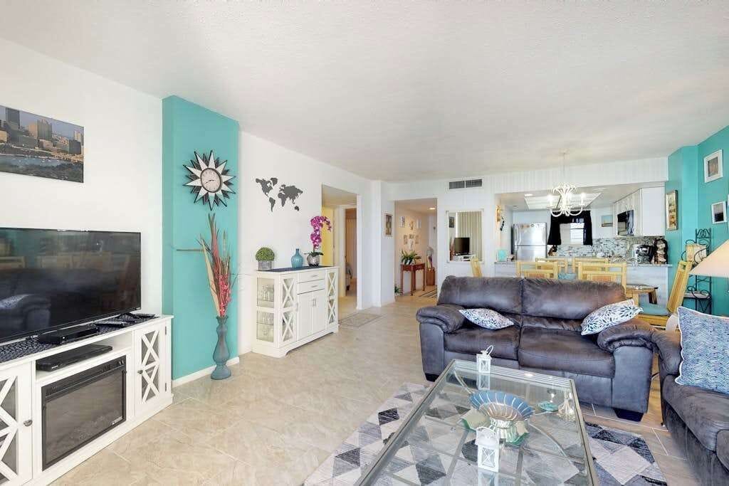 A living room with a television, sofa, and coffee table. There is a kitchen in the background.