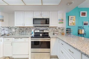 A kitchen with white cabinets, a microwave, an oven, and a granite countertop. - Oceanfront Arcadian II  8D (Myrtle Beach)