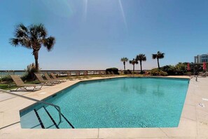 A clear blue pool with lounge chairs and palm trees, surrounded by a fence and a clear sky. - Oceanfront Arcadian II  8D (Myrtle Beach)