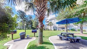 Un'area del parco con una palma, tavoli da picnic e un edificio sullo sfondo.