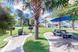 Ein Park mit einer Palme, Picknicktischen und einem Gebäude im Hintergrund.