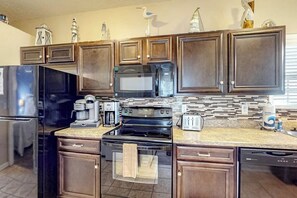 A kitchen with dark wooden cabinets, a stainless steel refrigerator, a microwave, a stove, and a dishwasher. - Palm Tree Paradise Beach Cottage (Myrtle Beach)