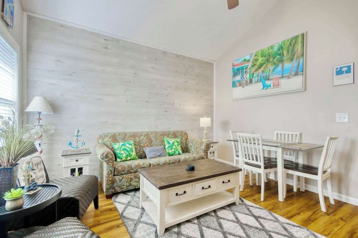A living room with a sofa, coffee table, dining table, chairs, and a painting on the wall.
