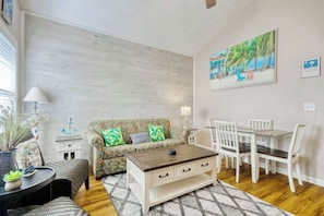 Ein Wohnzimmer mit Sofa, Couchtisch, Esstisch, Stühlen und einem Bild an der Wand.
