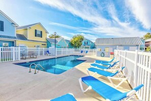 A swimming pool with lounge chairs and a white fence. - Palm Tree Paradise Beach Cottage (Myrtle Beach)