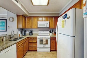 A kitchen with wooden cabinets, a white stove, a microwave, and a refrigerator. - Pelicans Watch 106 On the Beach (Myrtle Beach)