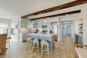 A modern kitchen with a large island, bar stools, and a wooden ceiling beam. - Palmetto Sunrise Waterfront Condo (Litchfield Beach)